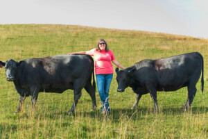 Lady standing in farm field in between two dark cows